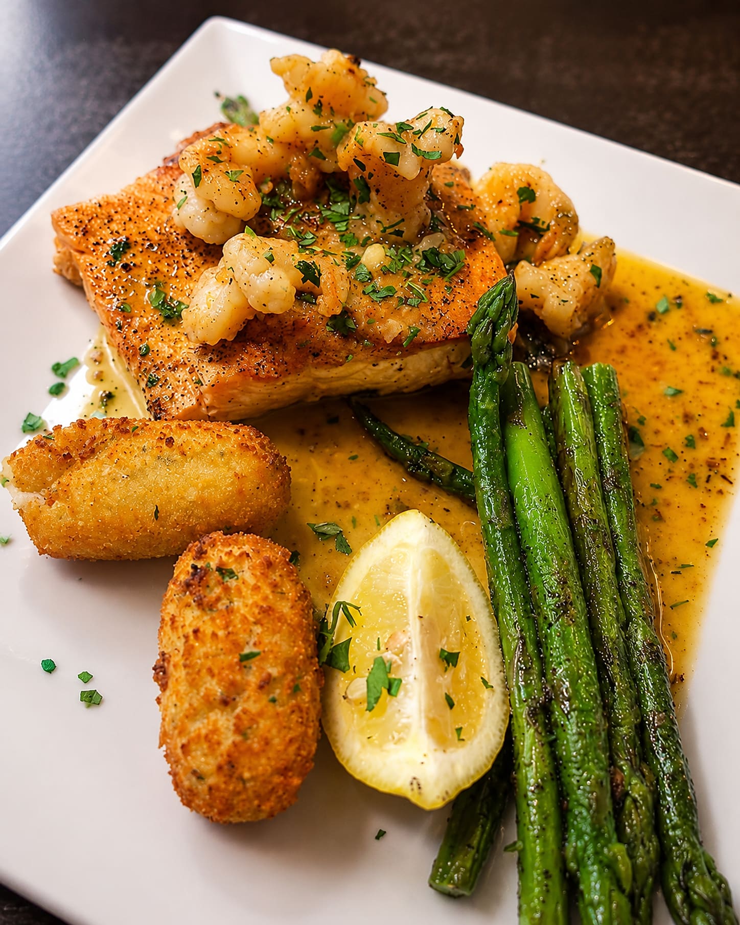 A fish fillet topped with shrimp in a butter sauce, with asparagus, a croquette and a wedge of lemon.